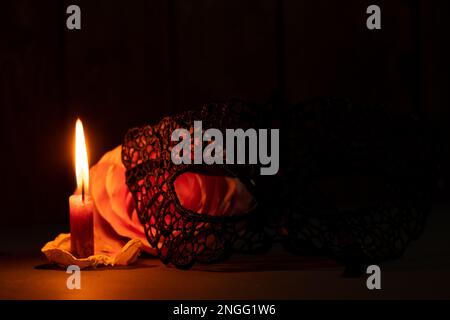 Eine Kerzenflamme und neben einer Rose in der dunklen Nahaufnahme Stockfoto