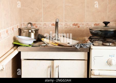Waschbecken voll, dreckiges Geschirr und ein Gasherd in der Küche im Apartment Stockfoto