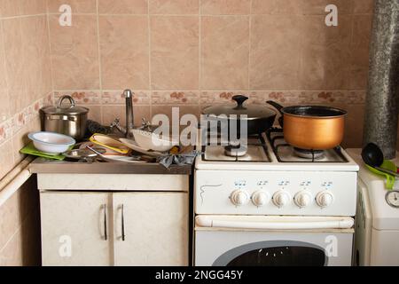 Waschbecken voll, dreckiges Geschirr und ein Gasherd in der Küche im Apartment Stockfoto