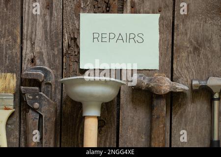 Gasschraubenschlüssel Hammerkolben und Bürste liegen auf einem Holztisch in der Küche und das Wort auf Papier in englischer Reparatur, Reparatur Stockfoto