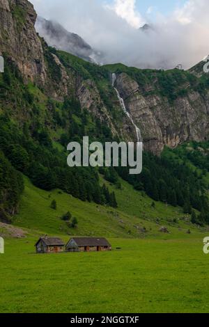 Zwei Bauernhäuser zwischen Bergen im Hintergrund ein Wasserfall Stockfoto