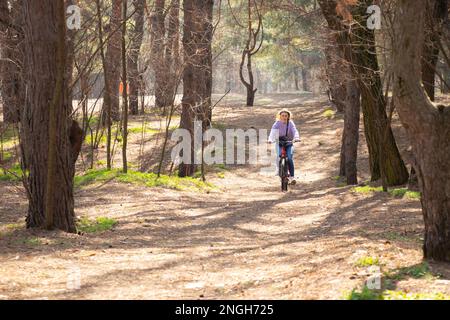 Mädchen fährt mit einem E-Bike im Frühlingswald in der Ukraine in der Stadt Dnipro, Outdoor-Erholung Stockfoto