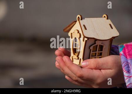 Die Kinderhand hält ein kleines Holzhaus auf einem verschwommenen Hintergrund Stockfoto