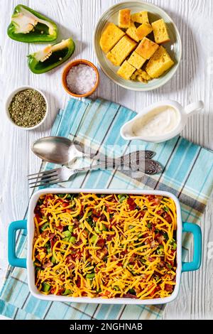 pinto Beans Speck Maisbrotsalat mit Tomaten, Paprika, Mais und Cheddar Käse in rechteckiger Schüssel auf weißem Holztisch mit Löffel und Gabel, vertica Stockfoto