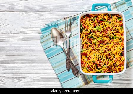 pinto Beans Speck Maisbrotsalat mit Tomaten, Paprika, Mais und Cheddar Käse in rechteckiger Schüssel auf weißem Holztisch mit Löffel und Gabel, Horizont Stockfoto