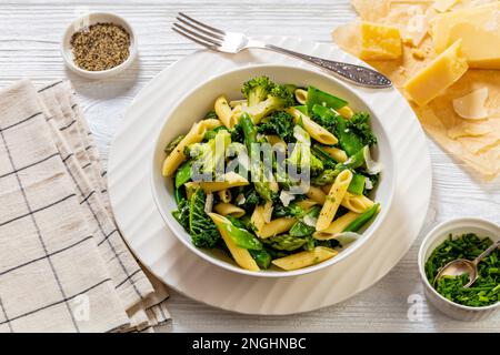 Pasta primavera mit Spargel, Erbsen, Brokkoli und Grünkohl in weißer Schüssel, auf weißem Holztisch Stockfoto