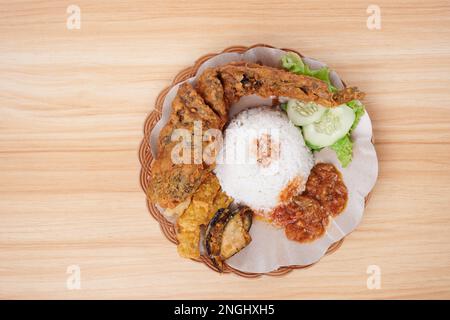 Gebratener Catfish mit scharfer Sauce, Reis und Gemüse auf einem Teller (Pecel Lele) Stockfoto