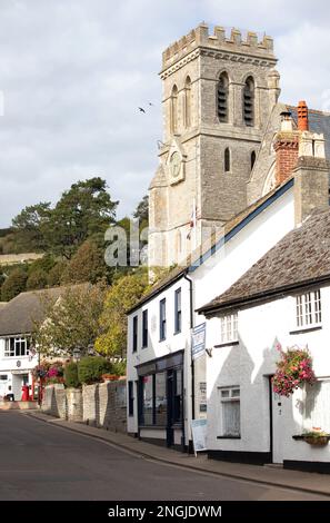 Die Kirche und die weiß getünchten Geschäfte in der Hauptstraße im malerischen Fischerdorf Beer in Devon, England. Stockfoto