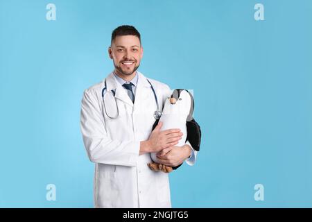 Kinderarzt mit Spielzeugpinguin und Stethoskop auf hellblauem Hintergrund Stockfoto