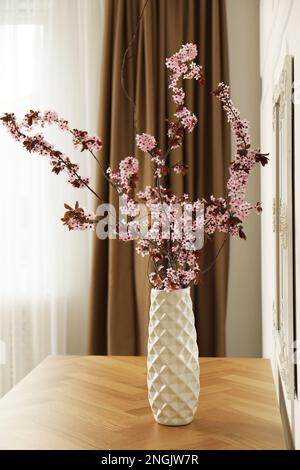 Blühende Baumzweige in Vase auf Holztisch im Innenbereich Stockfoto