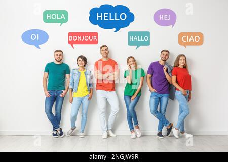 Fröhliche Leute, die neben einer hellen Wand posieren und Sprechblasen mit dem Wort „Hallo“ in verschiedenen Sprachen illustrieren Stockfoto