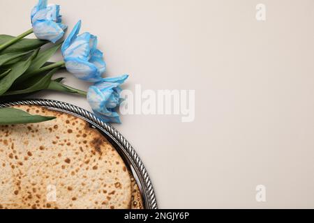 Schmackhafte Matzen und frische Tulpen auf hellgrauem Hintergrund, flach liegend mit Platz für Text. Pessach-Feier Stockfoto