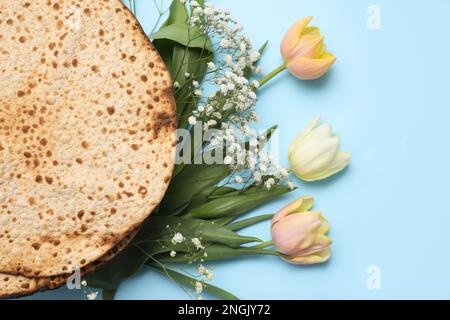 Leckere Matzen und frische Blumen auf hellblauem Hintergrund, flach liegend. Pessach-Feier Stockfoto