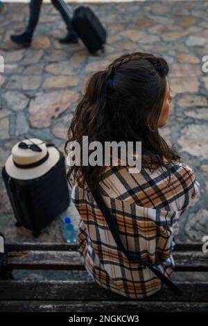 An einem sonnigen Tag sitzt eine wunderschöne Touristin auf einer Bank. Sie macht eine Pause Stockfoto