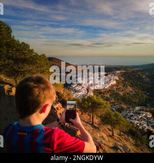 Ein kleiner Junge, der mit einem Smartphone Frigiliana Village von oben fotografiert, Malaga Province, Andalusien, Spanien Stockfoto