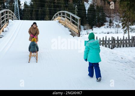 Drei Kinder, die mit einer kleinen Schwester auf einem Holzschlitten zum Schneepflug fahren Stockfoto