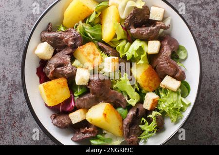 Köstlicher französischer Salat mit Muskelmagen, Kartoffeln, Salat, Zwiebeln und Croutons auf einem Teller auf dem Tisch. Horizontale Draufsicht von oben Stockfoto