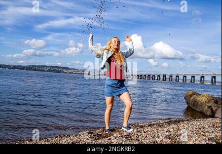 An einem wunderschönen Oktobertag in Wormit Beach, Fife, wirft Rhianna Martin Kiesel über ihren Kopf in den Fluss Tay, Schottland Stockfoto