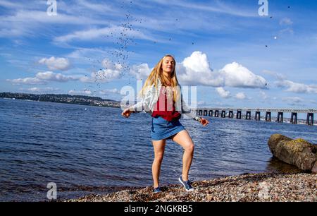 An einem wunderschönen Oktobertag in Wormit Beach, Fife, wirft Rhianna Martin Kiesel über ihren Kopf in den Fluss Tay, Schottland Stockfoto
