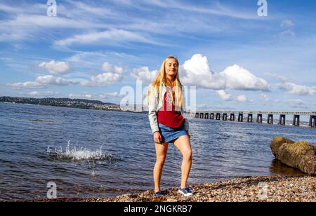 An einem wunderschönen Oktobertag in Wormit Beach, Fife, wirft Rhianna Martin Kiesel über ihren Kopf in den Fluss Tay, Schottland Stockfoto