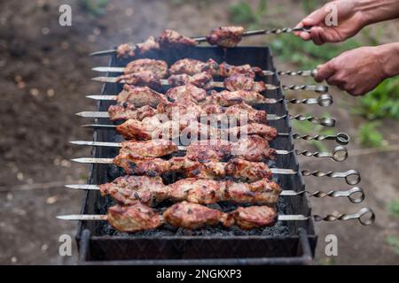 Er wirft den gebratenen Shish Kebab auf den Grill, mit den Händen an den Spießen. Geringe Schärfentiefe Stockfoto