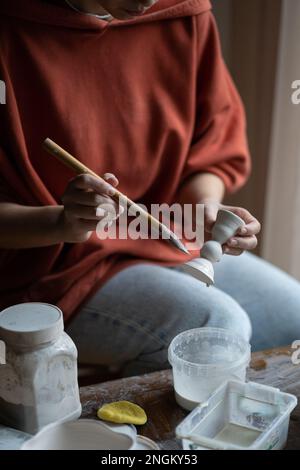 Craft Woman hält Tonprodukte, die mit Pinsel und Wasser hergestellt wurden, um die Verbindung von Keramikmaterial zu glätten. Stockfoto