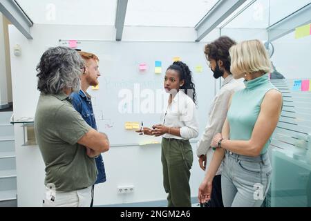 Treffen kreativer Kollegen im Büro, um dem Gruppenleiter zuzuhören und das Whiteboard zu betrachten. Stockfoto
