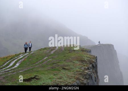 Edinburgh, Schottland, Großbritannien. 18. Februar 2023 Die Menschen gehen unter dem bleigrauen Himmel spazieren, während niedriger Nebel und hartnäckiger Nieselregen die Salisbury Crags im Holyrood Park umhüllen. Kredit: Craig Brown/Alamy Live News Stockfoto