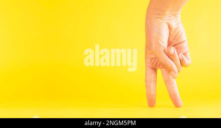 Eine Frauenhand, die Beine mit Fingern imitiert, humorvoll, wie aufrecht zu gehen, auf gelbem Hintergrund Stockfoto