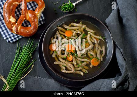 Bayerisches, schwäbisches und österreichisches Gericht: Leberspaetzle in einer Rindersuppe serviert mit knuspriger Brezel Stockfoto