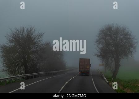 Containerlaster, der an einem nebeligen Tag auf einer konventionellen Autobahn fährt. Stockfoto