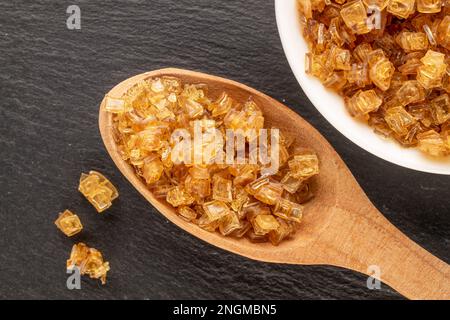 Gelbes Gelatinegranulat auf weißer Platte mit Holzlöffel auf Schieferstein, Makro, Draufsicht. Stockfoto