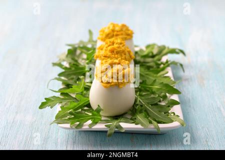 Gekochte Eier gefüllt mit gebratenen Zwiebeln und Kurkuma mit frischem Rucola auf hellblauem Hintergrund. Köstlicher hausgemachter Snack Stockfoto