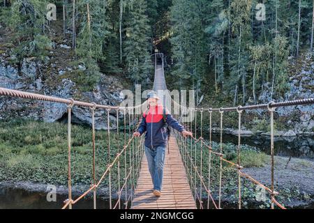 Lächelnder Senior-asiate auf einer Hängebrücke über den Hintergrund der Natur. Stockfoto