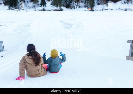 Zwei Mädchen, die sich darauf vorbereiten, den Schneehügel in den Bergen hinunter zu rutschen Stockfoto