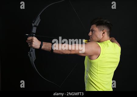 Mann mit Pfeil und Bogen, der Bogenschießen auf schwarzem Hintergrund praktiziert Stockfoto