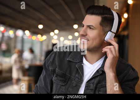 Attraktiver Mann mit Kopfhörern, der im Café draußen Musik hört, Platz für Text Stockfoto