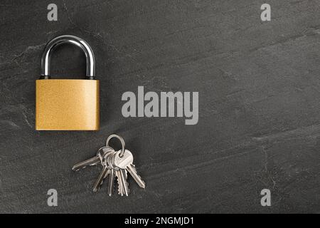 Modernes Vorhängeschloss mit Schlüsseln auf schwarzem Tisch, flach liegend. Platz für Text Stockfoto