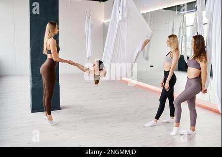 Junge Ausbilderin, die weibliche Gruppen-Stretching-Übungen an der Hängematte lehrt Stockfoto
