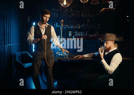 Ernsthafte Typen, die eine Hookah rauchen, während sie sich im Pub ausruhen Stockfoto