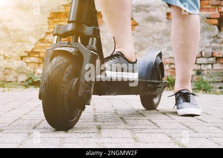 Beine einer nicht wiedererkennbaren Person mit elektrischem Kickroller oder E-Roller - E-Mobilität oder Mikromobilität Hipster Lifestyle-Konzept mit Sonnenschein Stockfoto