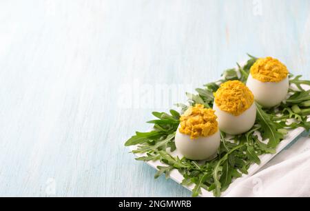 Gekochte Eier gefüllt mit gebratenen Zwiebeln und Kurkuma mit frischem Rucola auf hellblauem Hintergrund. Köstlicher hausgemachter Snack. Leerzeichen Stockfoto