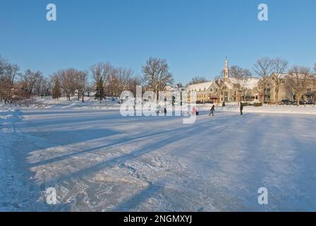 Jeunes qui patinent sur l'étang des Moulins gelé journée ensoleillée hiver. Kinder, die an einem sonnigen Tag auf einem gefrorenen Teich in Terrebonne skaten. Stockfoto