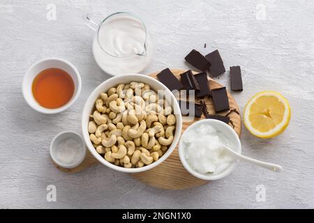 Zutaten für köstlichen veganen Schokoladen-Cashew-Käsekuchen: Cashews, Schokolade, Kokosnussöl, Kokosnusscreme, Jerusalem-Artischockensirup, Zitrone und Salz Stockfoto