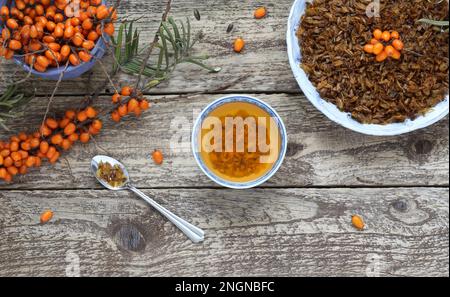 Seedorn-Tee. Zweig, frische und getrocknete Sanddornbeeren und eine Tasse heißes Getränk auf Holzhintergrund. Draufsicht. Gepresste getrocknete Sanddornberrie Stockfoto