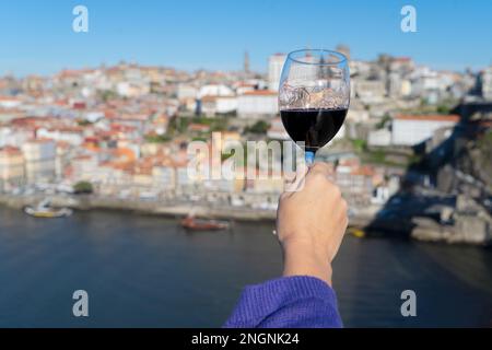 Hand einer Frau mit einem Glas rubinfarbenem Portwein in der historischen Stadt Porto, Hintergrund Portugal Stockfoto