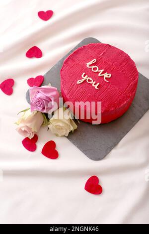 Leckerer roter Bento-Kuchen und Rosen liegen auf weißem Bett Stockfoto