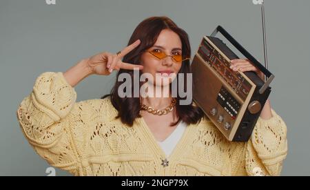 Glückliche Frau mit Sonnenbrille, die mit einem Retro-Plattenspieler Musik hört, Disco-Tanz oder Lieblingsmusik tanzt, Spaß hat, Unterhaltung hat, Fan von Vintage-Technologien ist. Junge Frau isoliert auf grauem Hintergrund Stockfoto