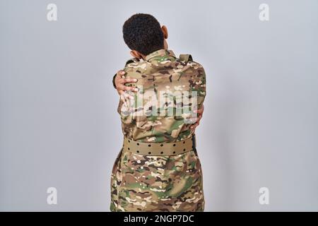 Wunderschöne afroamerikanische Frau in Tarnuniform, die sich glücklich und positiv umarmt. Selbstliebe und Selbstfürsorge Stockfoto