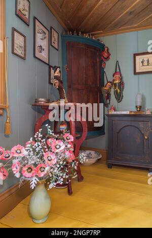Keramikvase mit pinkfarbenen Pfingstrosen und Beistelltisch und Eckschrank im oberen Hauptschlafzimmer mit gelb gestrichenen breiten Brettern. Stockfoto